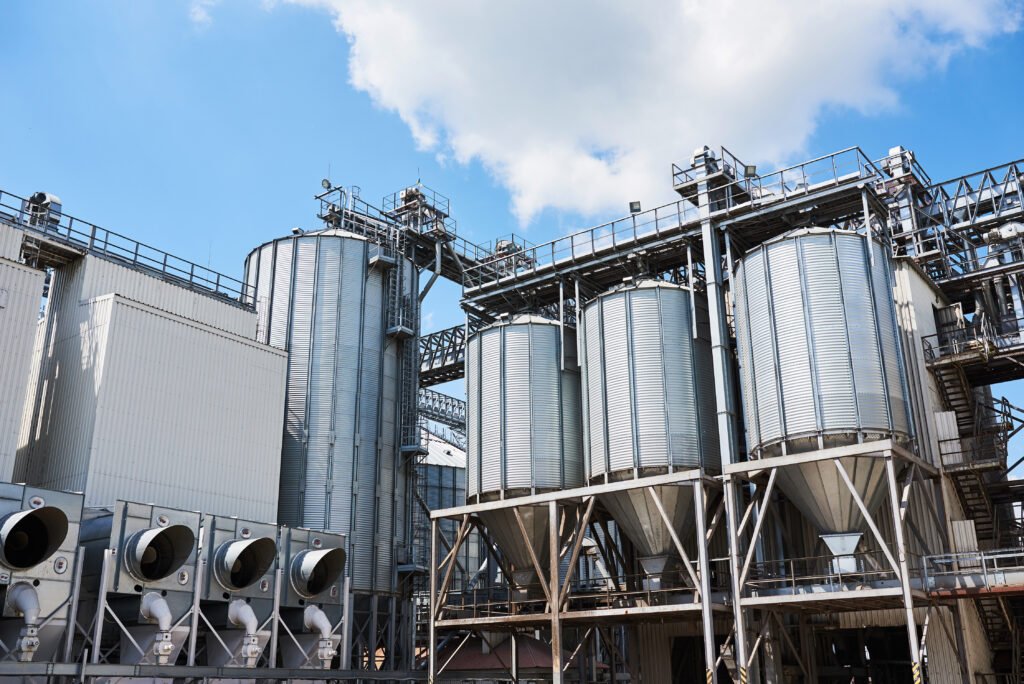 Agricultural Silos. Building Exterior. Storage and drying of grains, wheat, corn, soy, sunflower against the blue sky with white clouds.